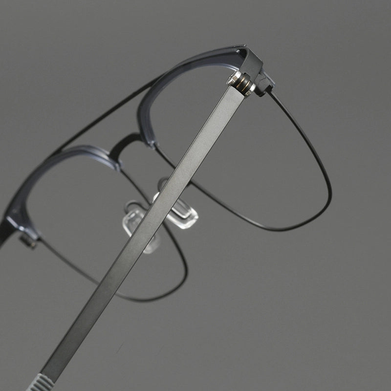 Close-up of a pair of browline designer glasses frames with a slim titanium gunmetal frame and thin black pure titanium temples, shown against a neutral gray background.