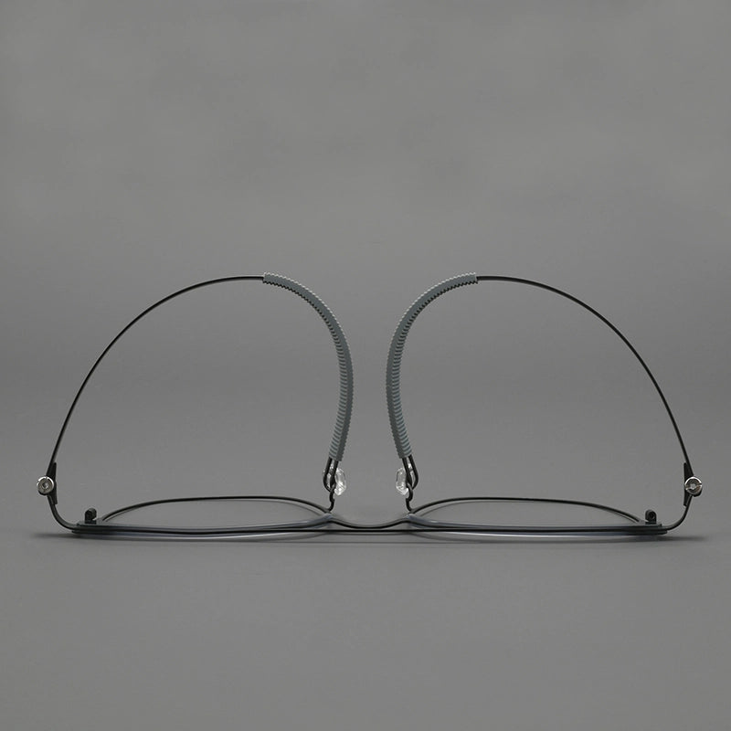 Thin black pure titanium eyeglass frames with adjustable nose pads, shown from the front on a neutral gray background.