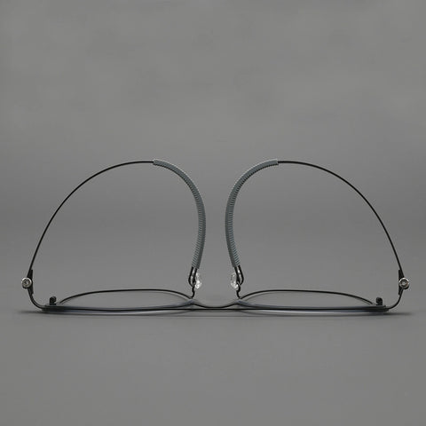 Thin black pure titanium eyeglass frames with adjustable nose pads, shown from the front on a neutral gray background.