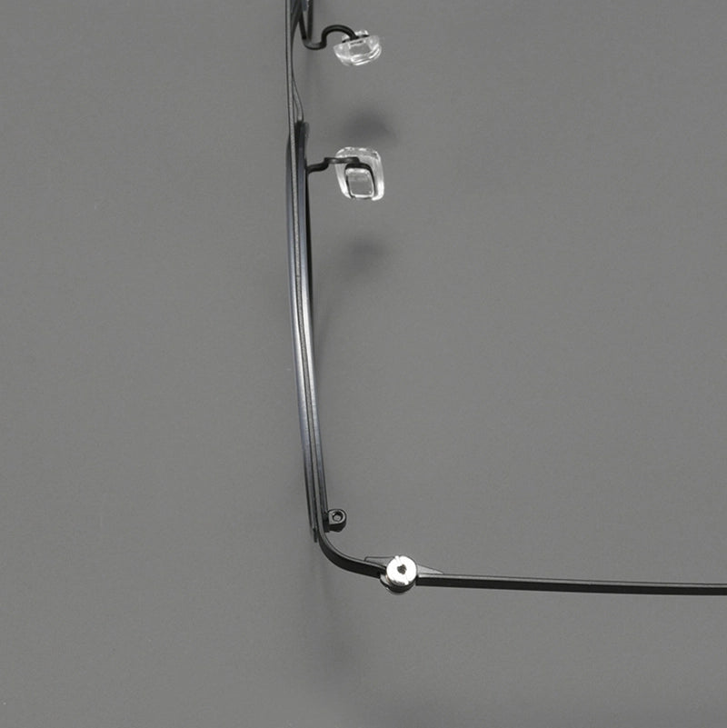Close-up of a pair of eyeglasses with a thin black pure titanium eyeglass frame, showing the temple arm, hinge, and clear adjustable nose pad against a solid gray background.