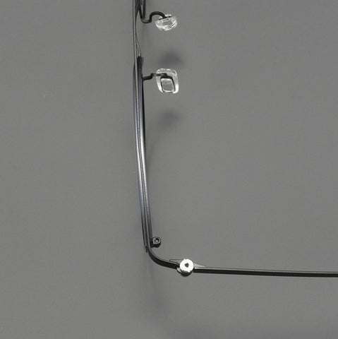 Close-up of a pair of eyeglasses with a thin black pure titanium eyeglass frame, showing the temple arm, hinge, and clear adjustable nose pad against a solid gray background.