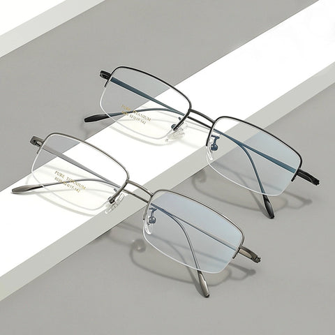 Two pairs of pure titanium half frame glasses for men from Verhalo Vision displayed on a clean, geometric gray and white background. One pair has a thin black metal frame, and the other has a thin silver metal frame, both with clear lenses.