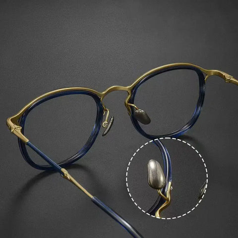 Round Vintage Designer Eyelasses from Verhalo Vision with a gold-tone frame and dark blue acetate detailing, shown on a dark gray background with a circular inset highlighting the hinge and pure titanium nose pad area.