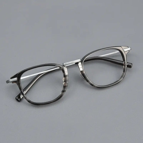 A pair of designer titanium eyeglasses with a dark gray and black marbled acetate front frame, silver titanium bridge and temples, and clear lenses, shown on a plain gay background.