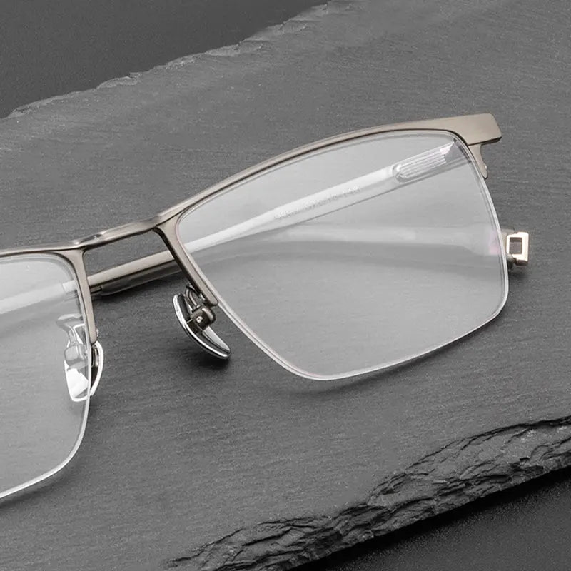 A pair of Pure Titanium Large Semi Rimless Spectacles for Men from Verhalo Vision with a matte silver metal frame and clear lenses, resting on a dark gray slate surface.