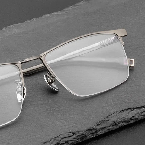 A pair of Pure Titanium Large Semi Rimless Spectacles for Men from Verhalo Vision with a matte silver metal frame and clear lenses, resting on a dark gray slate surface.