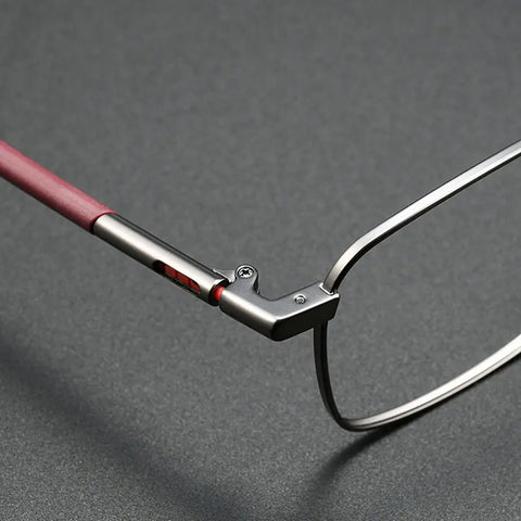 Close-up of a pair of Stylish Titanium Designer Eyewear from Verhalo Vision showing the hinge and temple arm, with a gunmetal pure titanium eyeglass frame and a reddish-brown TR90 temple tip on a textured dark gray background.