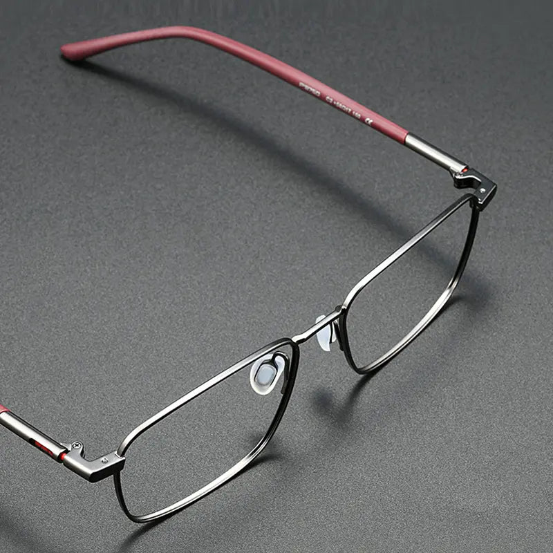 A pair of slim stylish titanium designer eyewear from Verhalo Vision with a dark gray titanium etyeglass frame and reddish temples, shown on a dark gray textured background.
