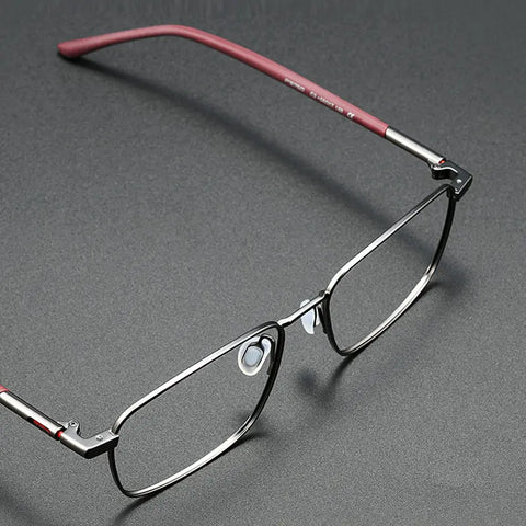 A pair of slim stylish titanium designer eyewear from Verhalo Vision with a dark gray titanium etyeglass frame and reddish temples, shown on a dark gray textured background.