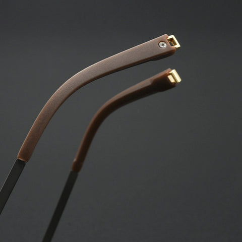 Close-up of two curved eyeglass temple arms with brown textured grips and gold metal tips, set against a dark gray background.