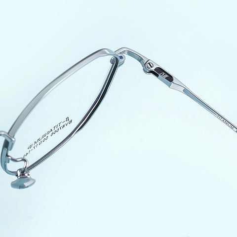 Close-up of a pair of thin titanium eyeglass frames on a pale blue background, showing the bridge, hinge, and temple arm with printed specifications.