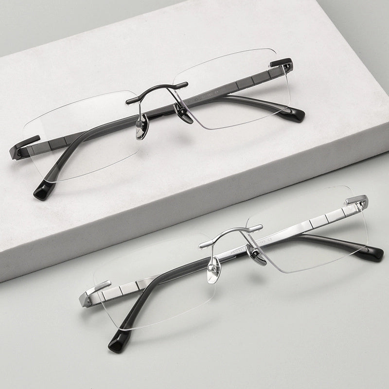 Two pairs of minimalist titanium rimless spectacles for Men on a light gray surface with a white box in the background.