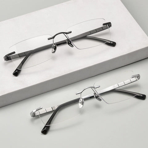 Two pairs of minimalist titanium rimless spectacles for Men on a light gray surface with a white box in the background.
