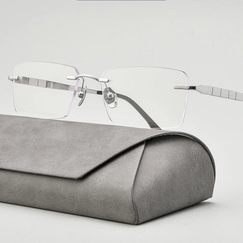 minimalist silver titanium rimless spectacles for men with silver titanium temples resting on a gray textured case against a light gray background.