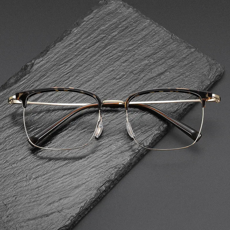 A pair of Browline Designer Pure Titanium Eyeglasses with a tortoiseshell acetate front and silver-toned metal bridge, resting on a dark gray slate block.