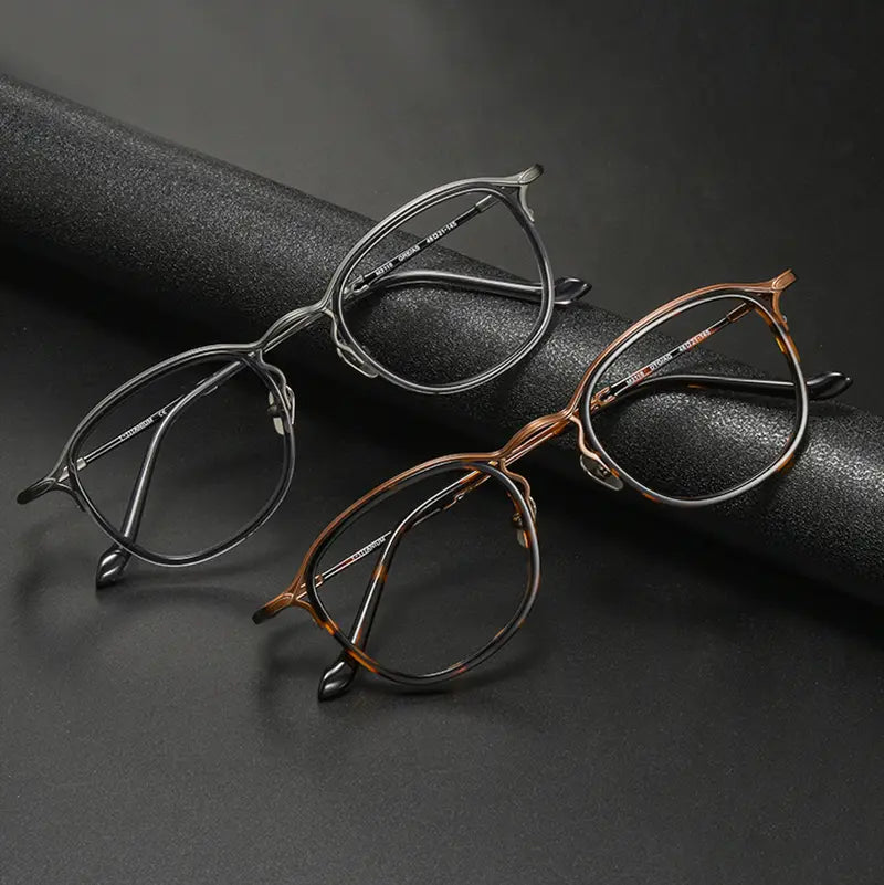Two pairs of pure titanium vintage designer eyelasses from Verhalo Vision displayed on a dark textured surface, one in matte black and one in warm bronze-brown with darker tortoiseshell-like detailing.