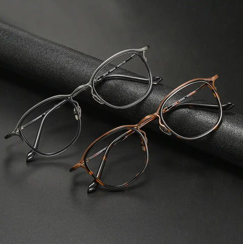 Two pairs of pure titanium vintage designer eyelasses from Verhalo Vision displayed on a dark textured surface, one in matte black and one in warm bronze-brown with darker tortoiseshell-like detailing.